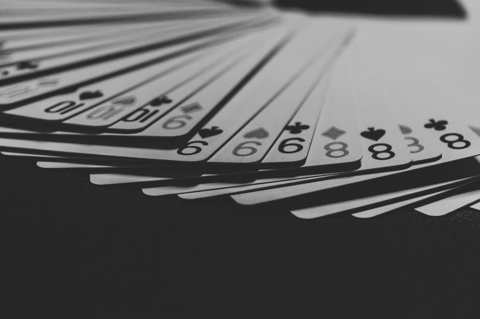 A grayscale close-up of a single playing card fanned out among others on a dim tabletop.