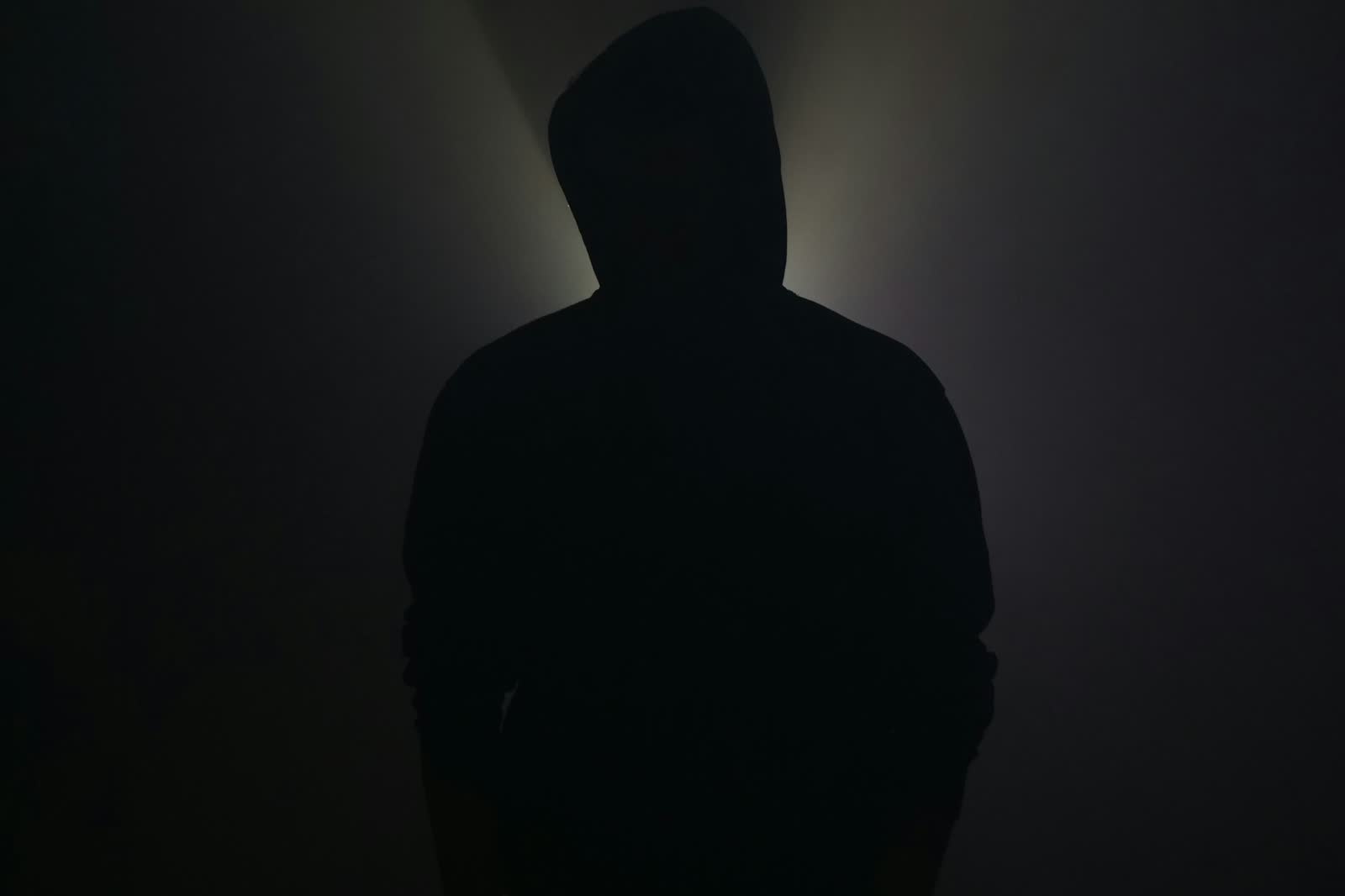 A single silhouetted figure standing illuminated in one pool of light, surrounded by darkness on all sides.