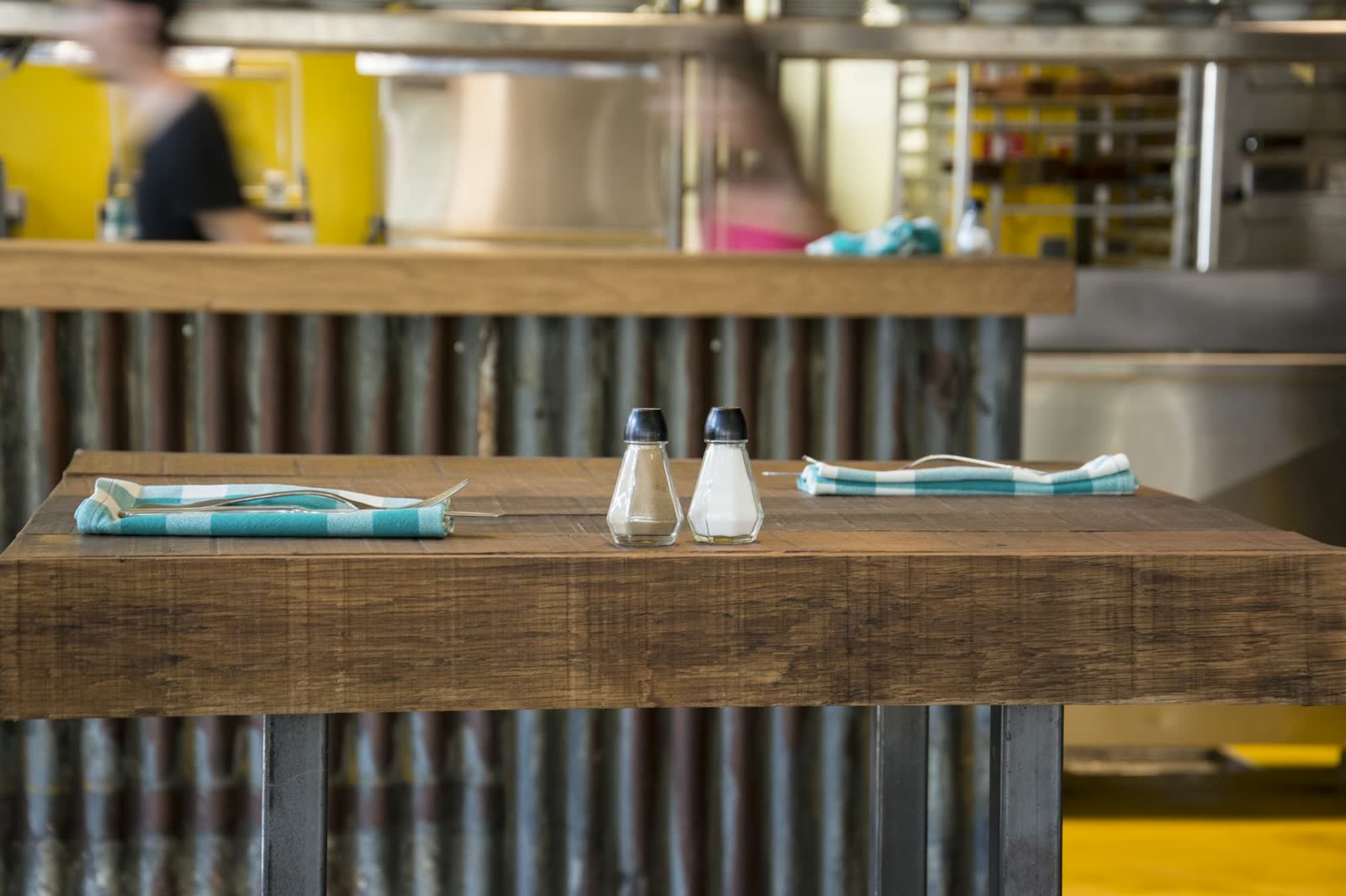 A pair of salt and pepper shakers standing on a warm brown wooden table, softly lit, in a minimalist dining setting.