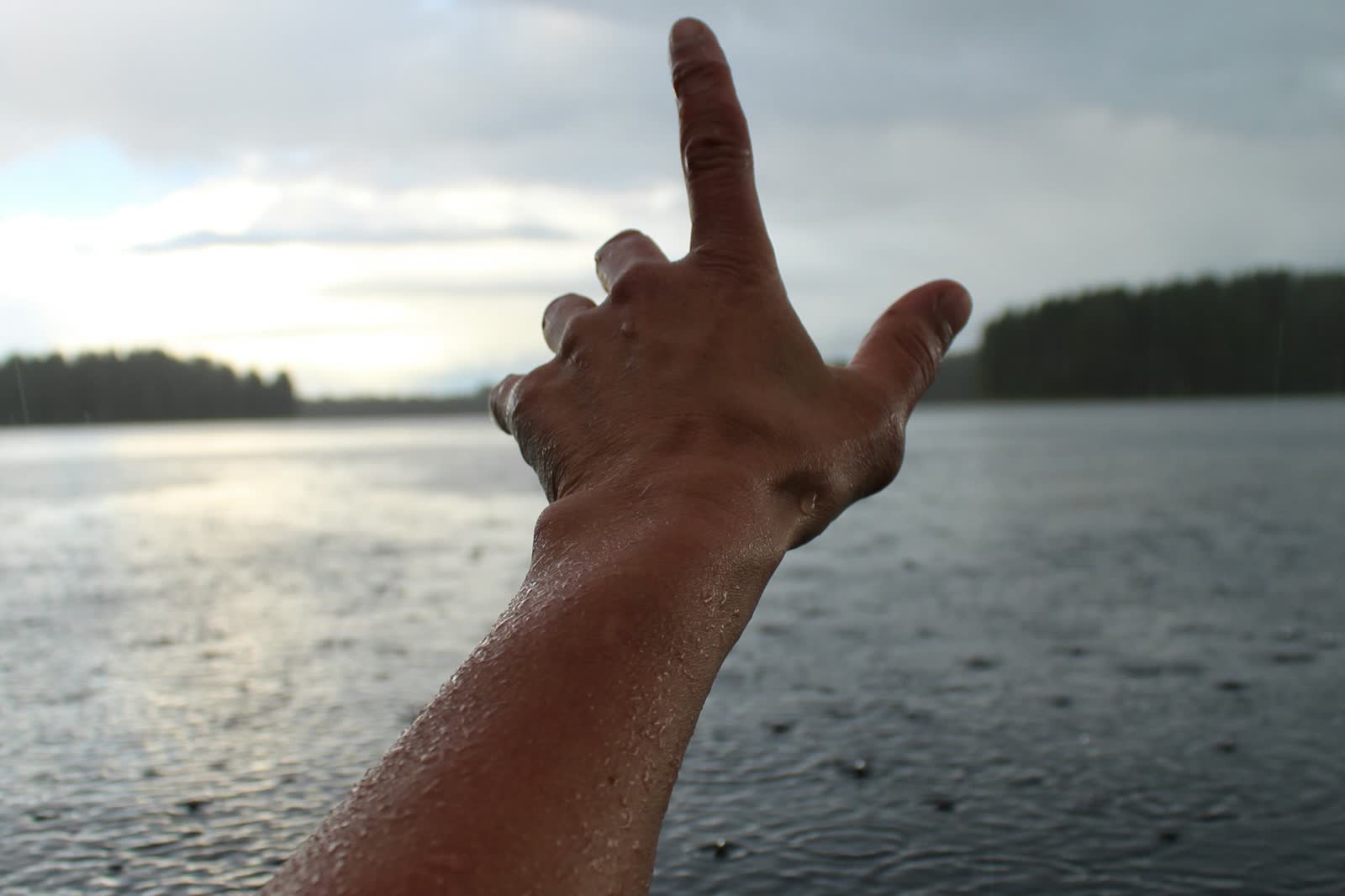A person's hand reaching out toward the surface of calm water, fingertips just touching the waterline.